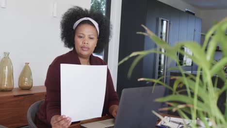 Mujer-Afroamericana-De-Talla-Grande-Usando-Una-Computadora-Portátil-Y-Sosteniendo-Documentos,-Inalterada,-En-Cámara-Lenta