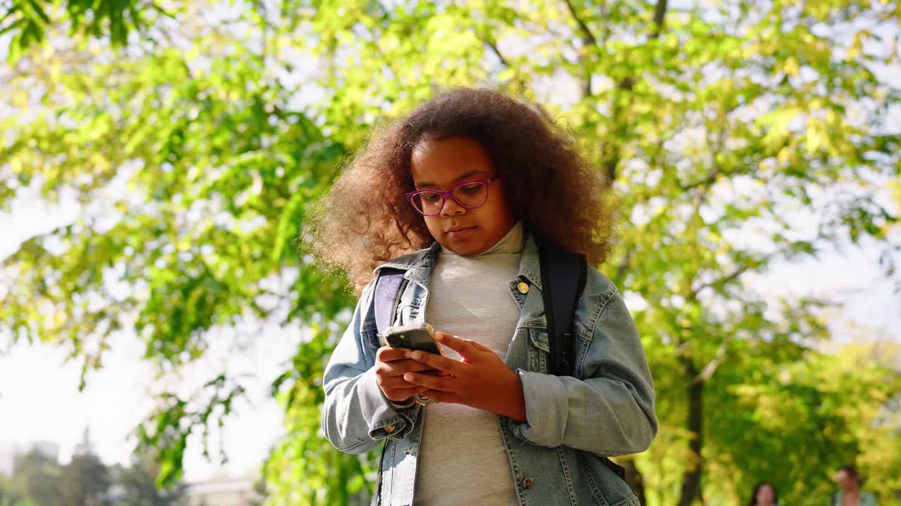 Young Girl with Curly Hair Using Smartphone in Sunny Park