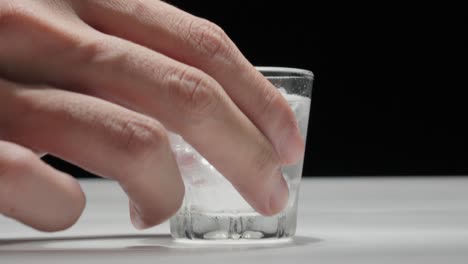 Hand-reaching-for-a-glass-of-water-with-ice-cubes-on-a-black-background,-high-contrast