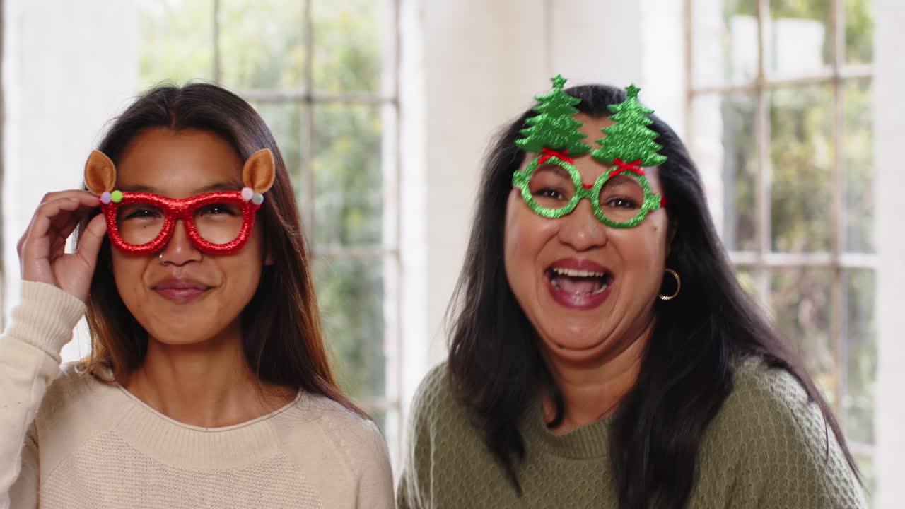 At christmas, Grandma and teenager wearing festive glasses, laughing together at home
