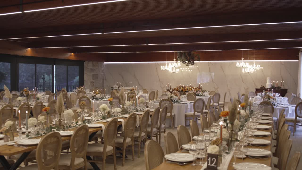 Breedbeeld van een stijlvolle bruiloftsreceptiehal met lange tafels, kroonluchters en bloemendecoratie.