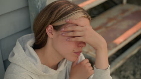 primer plano de una mujer joven cubriendo su rostro con su mano, apareciendo profundamente en pensamiento, ella descansa su otra mano en su brazo, emanando un estado de ánimo contemplativo, el fondo muestra pasos desgastados