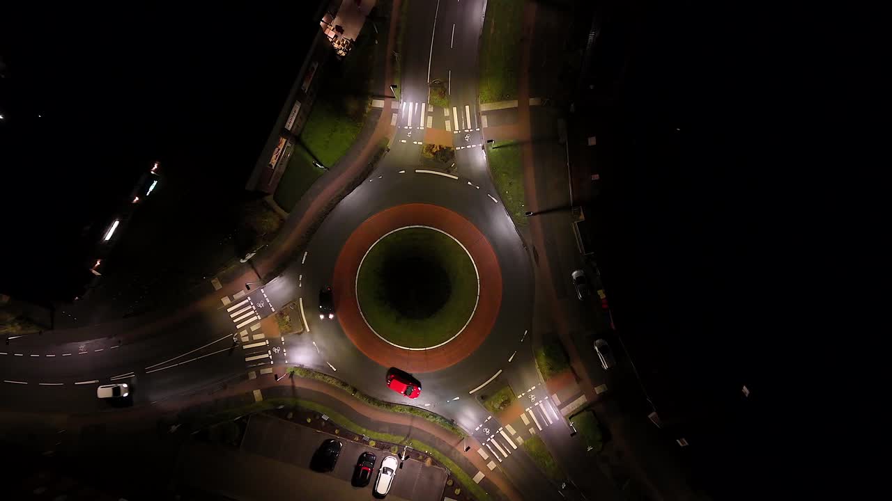 Traffic on illuminated roundabout of small american town. Nightscape in city with driving cars. Rising drone top down shot.
