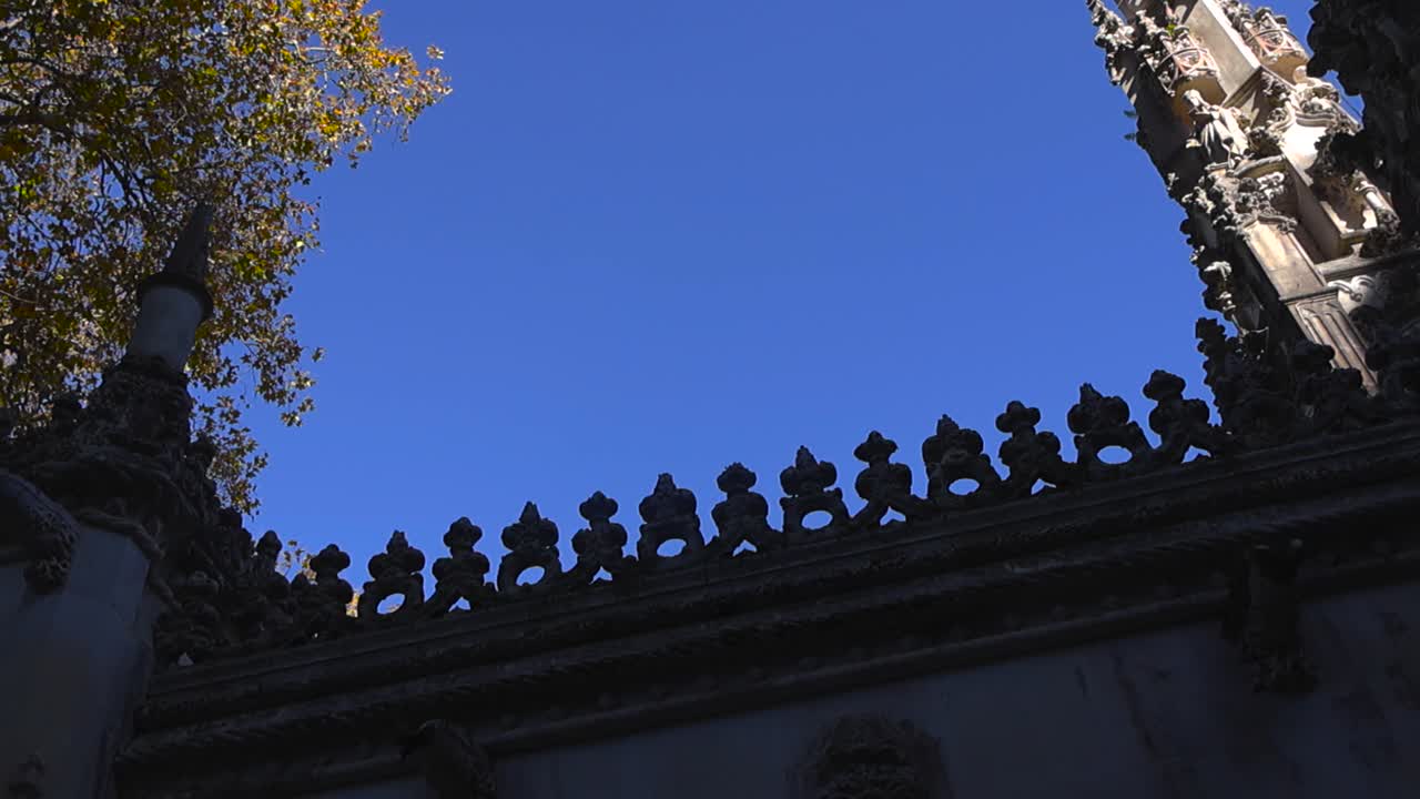 Vista verso l'alto di un'antica torre ornata e di opere in pietra decorative contro un cielo azzurro chiaro