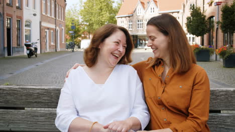 two happy women laughing on a bench in an old european town