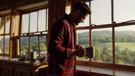 man drinks coffee while admiring the scenic view from a rustic cabin window