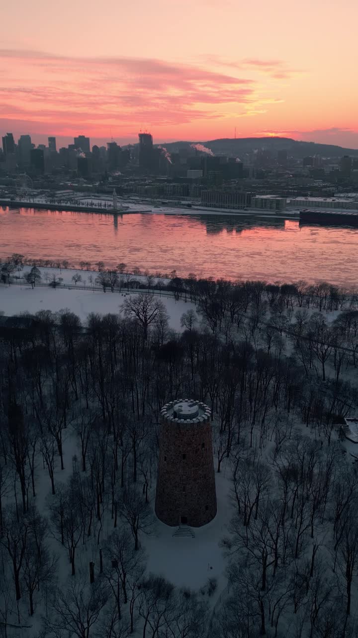 aerial vertical shot around Levis tower in Jean Drapeau Parc with Montreal city in the background at sunset during winter season, Quebec province, anada