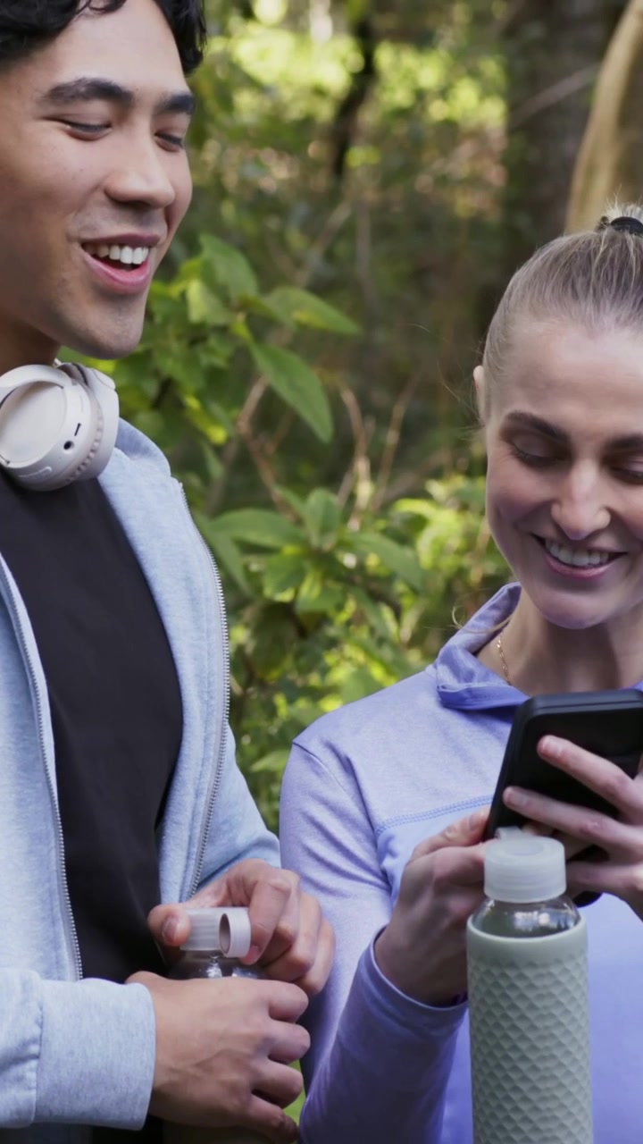 Vertical video: Turning phone, woman in athletic wear showing man funny clip at park, sharing laugh