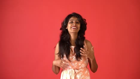 A-young-Indian-girl-in-orange-frock-controlling-her-laugh-standing-in-an-isolated-red-background