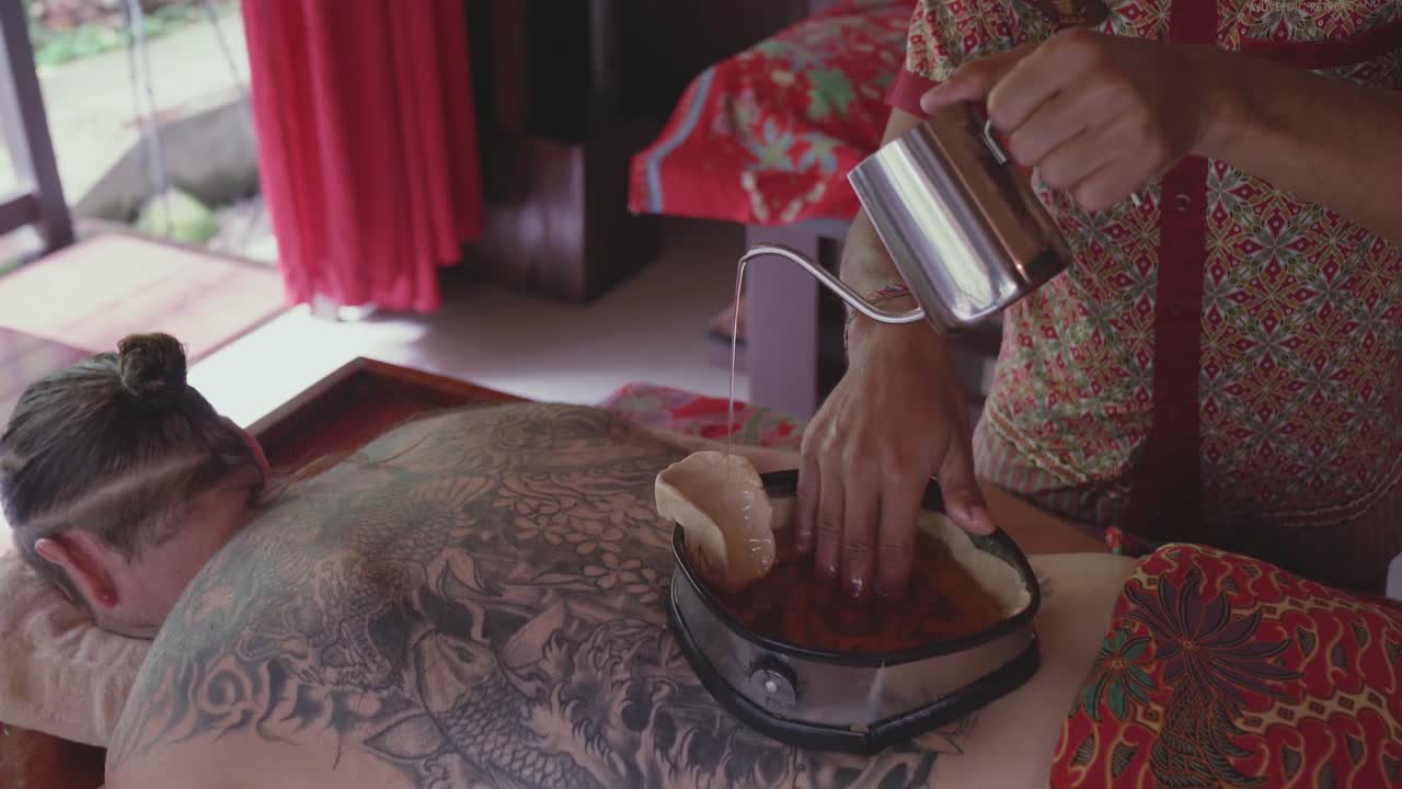 Il terapista della spa versa olio caldo in un contenitore rivestito di cera sulla schiena di un paziente uomo che si gode un trattamento ayurvedico Kati Vasti e lo mescola con la mano.
