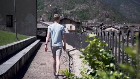 man in shorts and a t-shirt walking beside an old fence overlooking a typical picturesque old italian village