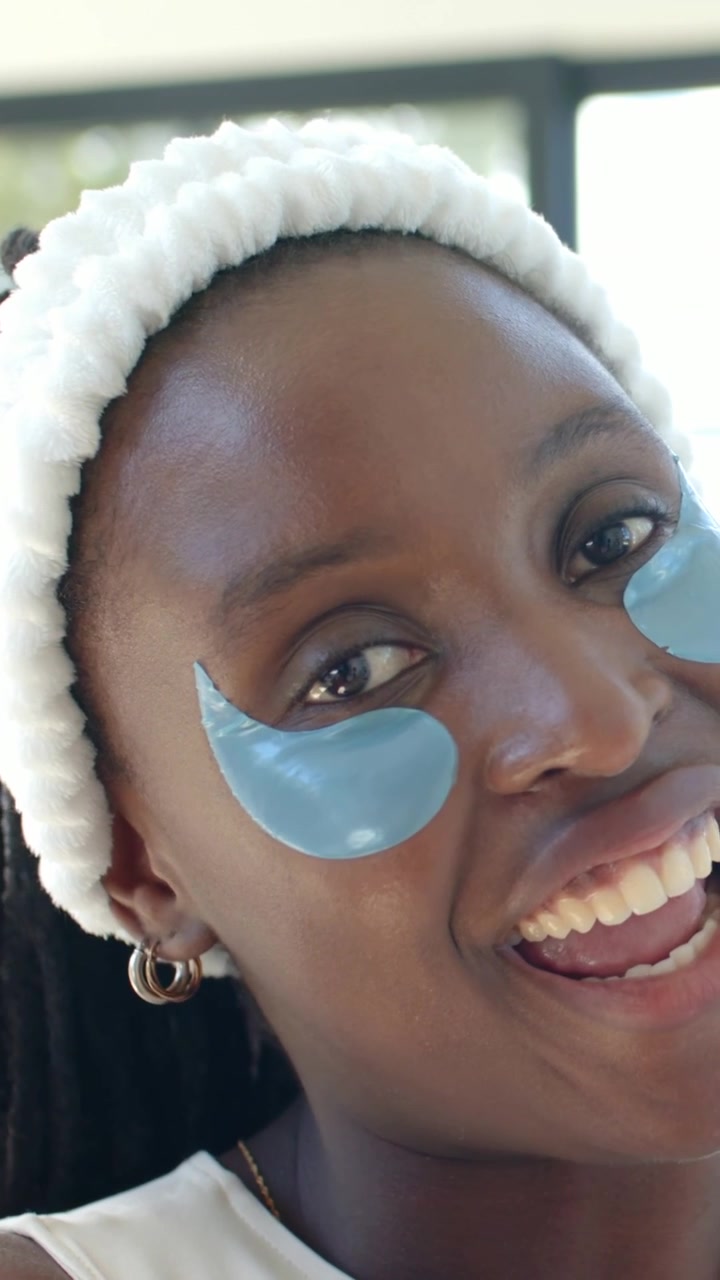 Vertical video: Speaking woman wearing headband and showing blue patches by window, camera starting