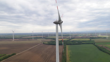 Slow-motion-aerial-of-a-wind-turbine-revolving-and-generating-green-energy,-winf-farm-in-background