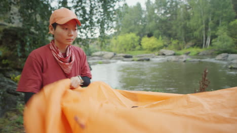 asian tourist preparing tent for camping on river bank