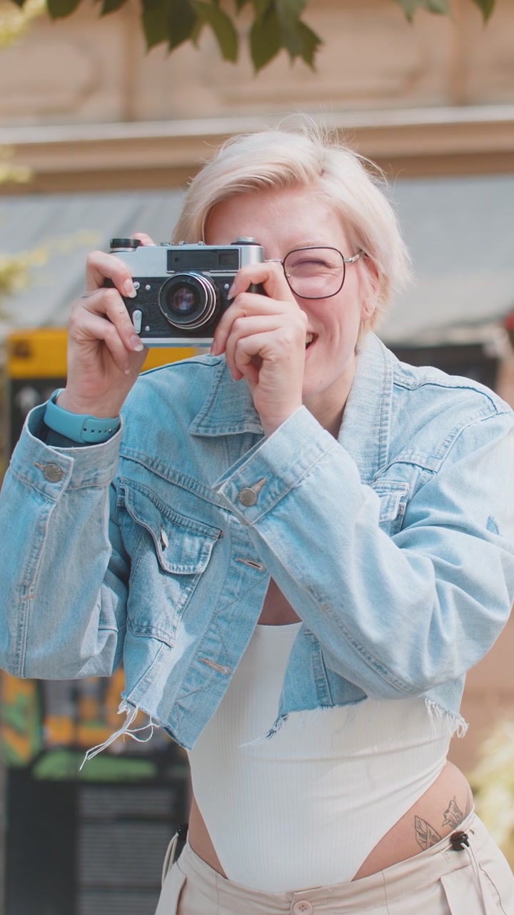 Felice giovane donna bionda caucasica turista che scatta foto con una macchina fotografica retrò in una strada urbana.