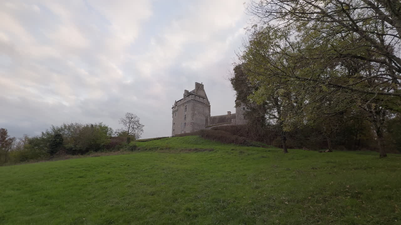 Historic Château du Bouchet in rural France surrounded by green fields under a cloudy sky