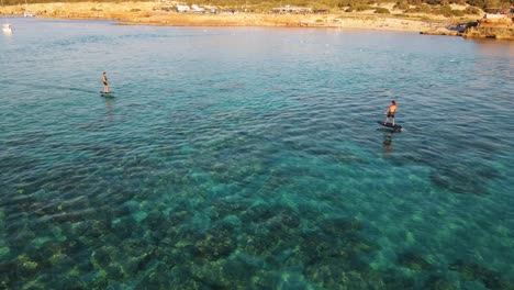 Aerial-shot-of-people-surfing-with-eFoil-electric-surfboards-at-Cala-Escondida-in-Ibiza,-Spain