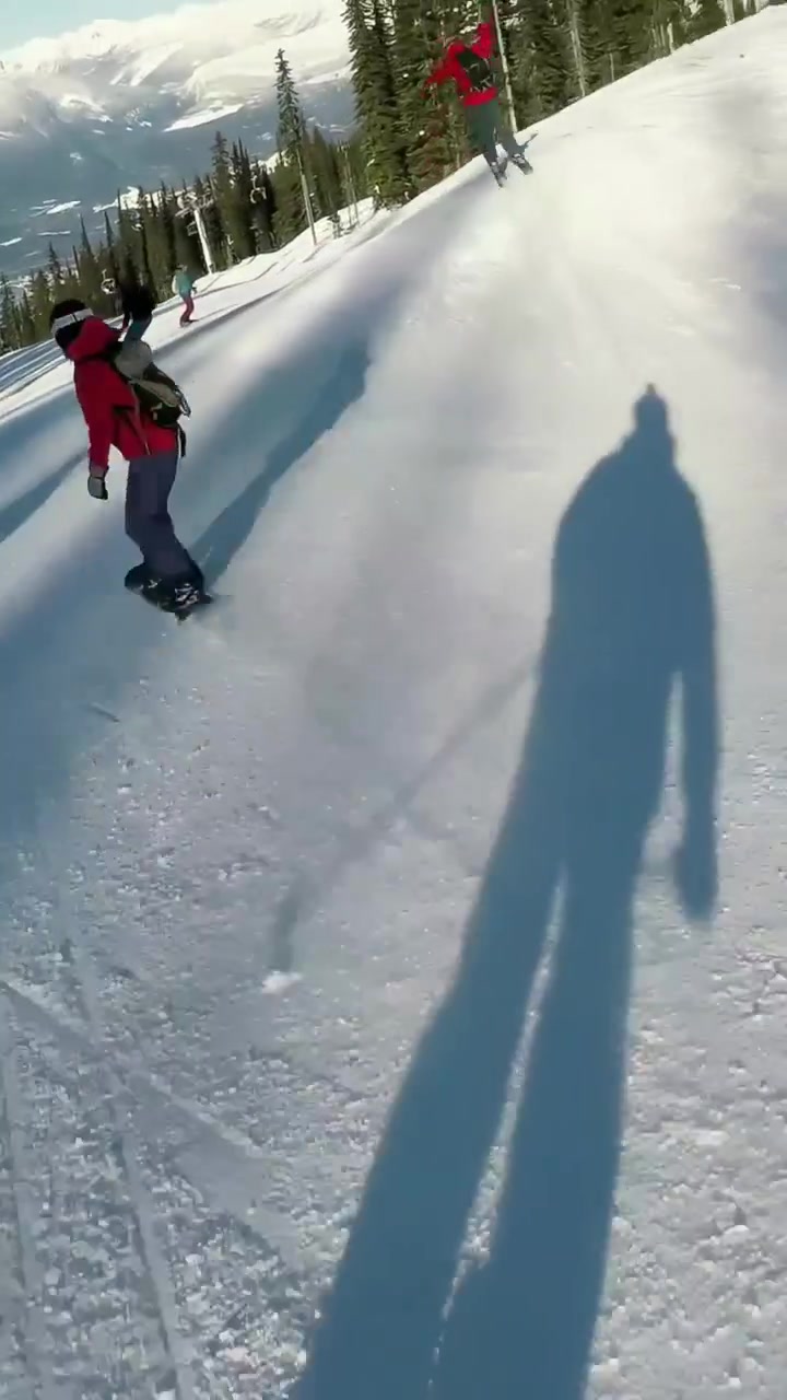 Video verticale: Snowboarder in giacca rossa che fa carving su pista battuta, affiancato da sciatori, con spazio per il testo.