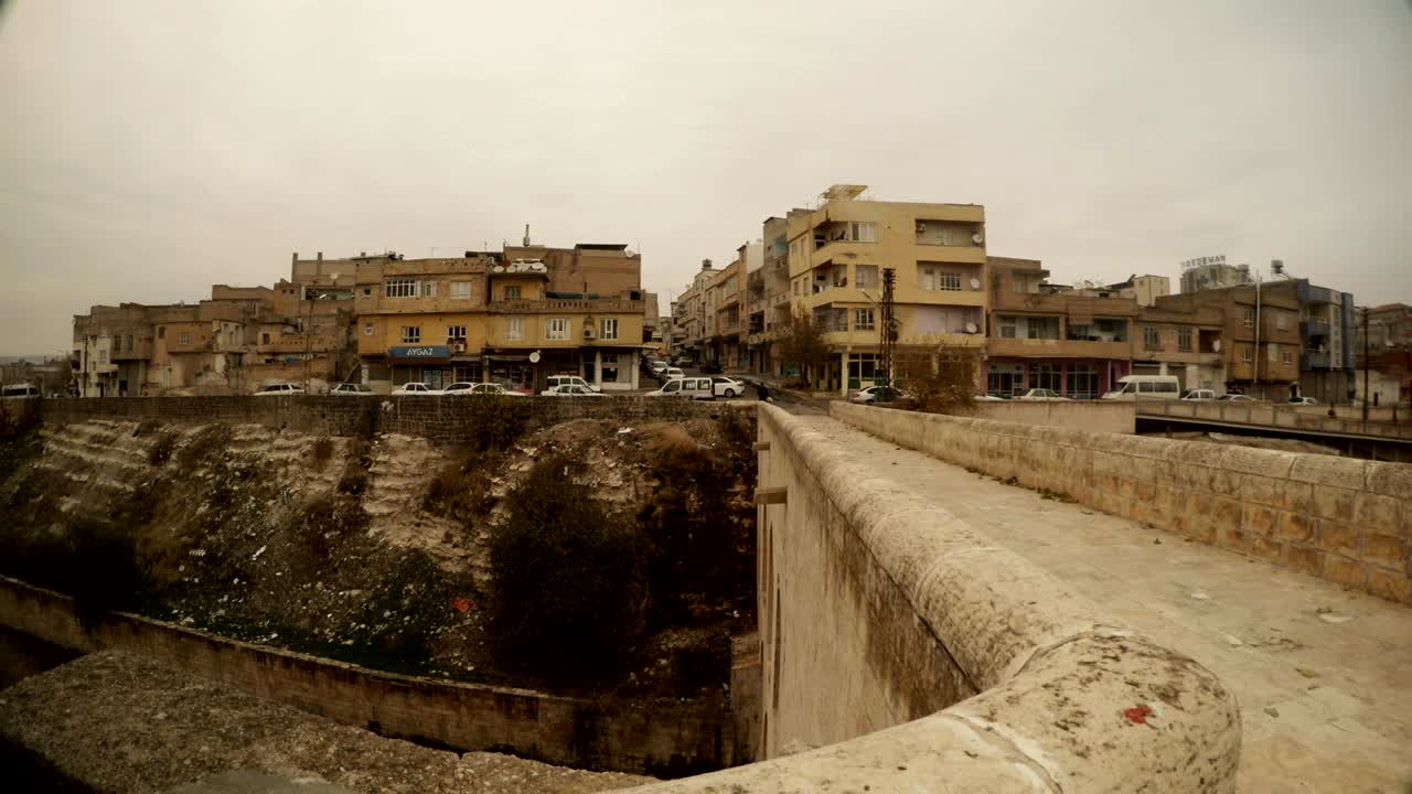 motocicleta cruza el viejo puente bajo el canal área residencial en el lado opuesto urfa