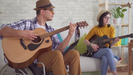 young man is a disabled musician in a wheelchair player and a young woman in glasses and a hat playing the guitar