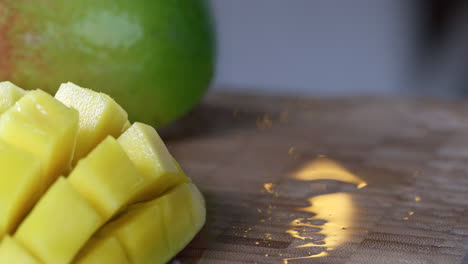 un mango cortado por la mitad, en rodajas y volteado al revés se presenta frente a un mango entero