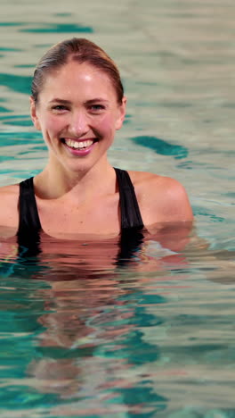 vertical video of fit woman doing aqua aerobics in the pool with foam dumbbells in the leisure cente