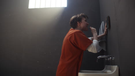 female inmate brushing her teeth by sink in prison cell