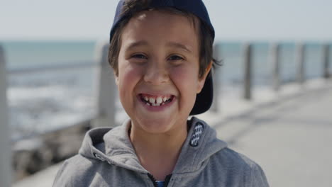 portrait of young hispanic boy smiling cheerful  enjoying summer day on seaside beach wearing hat