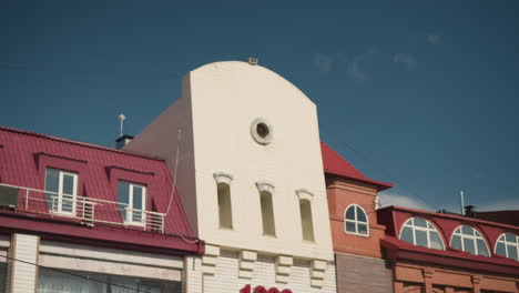 facade of an urban building with a white central tower, circular window, and red roof under a bright blue sky, architectural details highlight modern design in a serene cityscape setting