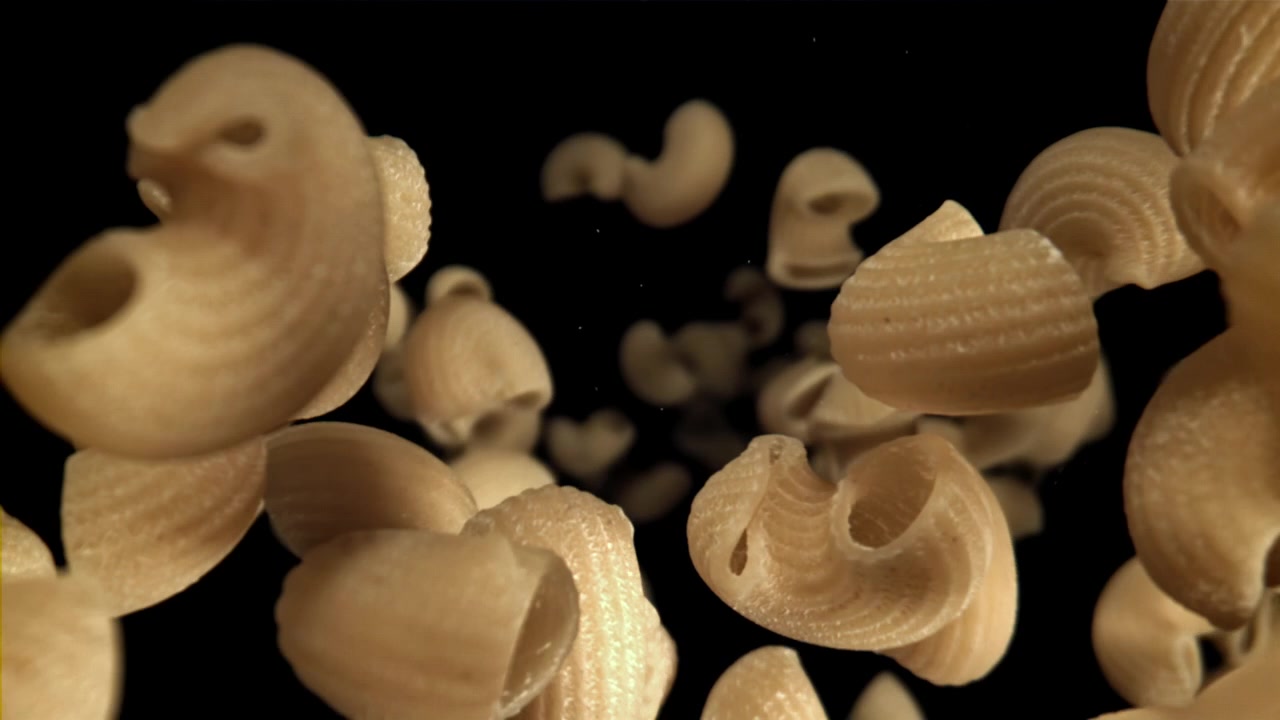 Pasta maccheroni cruda che cade al rallentatore su sfondo nero