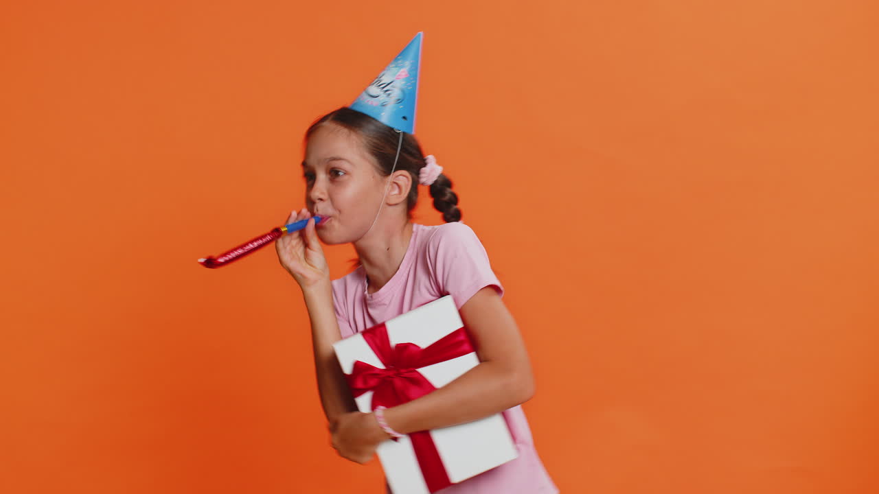 Felice e eccitata, fortunata ragazza che indossa un cappello di compleanno, un cono, un tubo da soffiare, che celebra il successo della festa, la vittoria della vittoria.