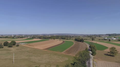 aerial view of amish countryside of farmer working field by a rail road track as a steam engine approaches as seen by a drone