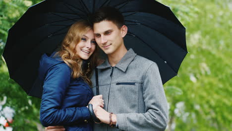 Ein-Liebevolles-Junges-Paar-Unter-Einem-Regenschirm-Wartet-Auf-Regen-HD-Video