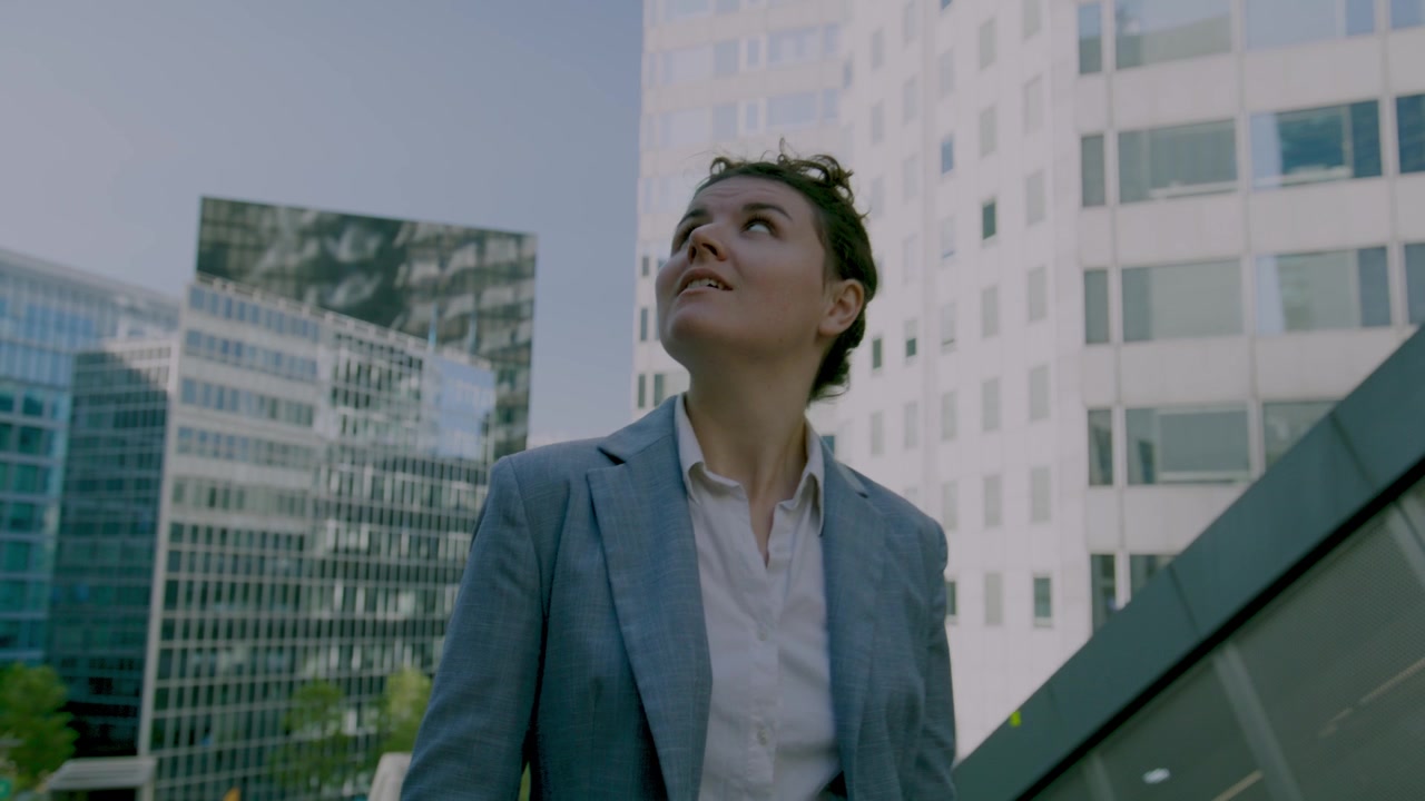 Mulher olhando para cima de forma aspiracional entre torres de escritórios, ângulo baixo, mulher de negócios, La Défense, corporativo, Paris, França, vídeo em HD, material de arquivo, b-roll, exterior, ao ar livre, durante o dia, luz natural
