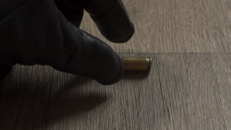 gloved criminal hand removing fired 9mm shell casing from living room floor and removing evidence from crime scene