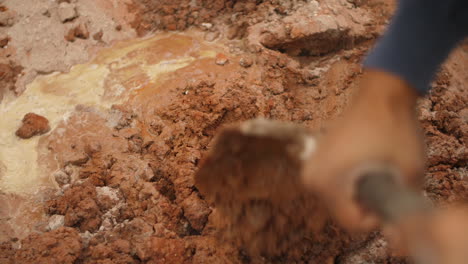 Construction-worker-mixing-cement-into-mud-with-spade