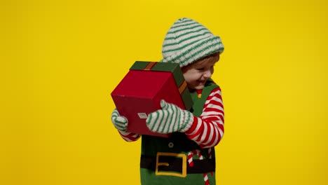 kid girl in christmas elf santa helper costume receiving present gift box. happy new year holidays