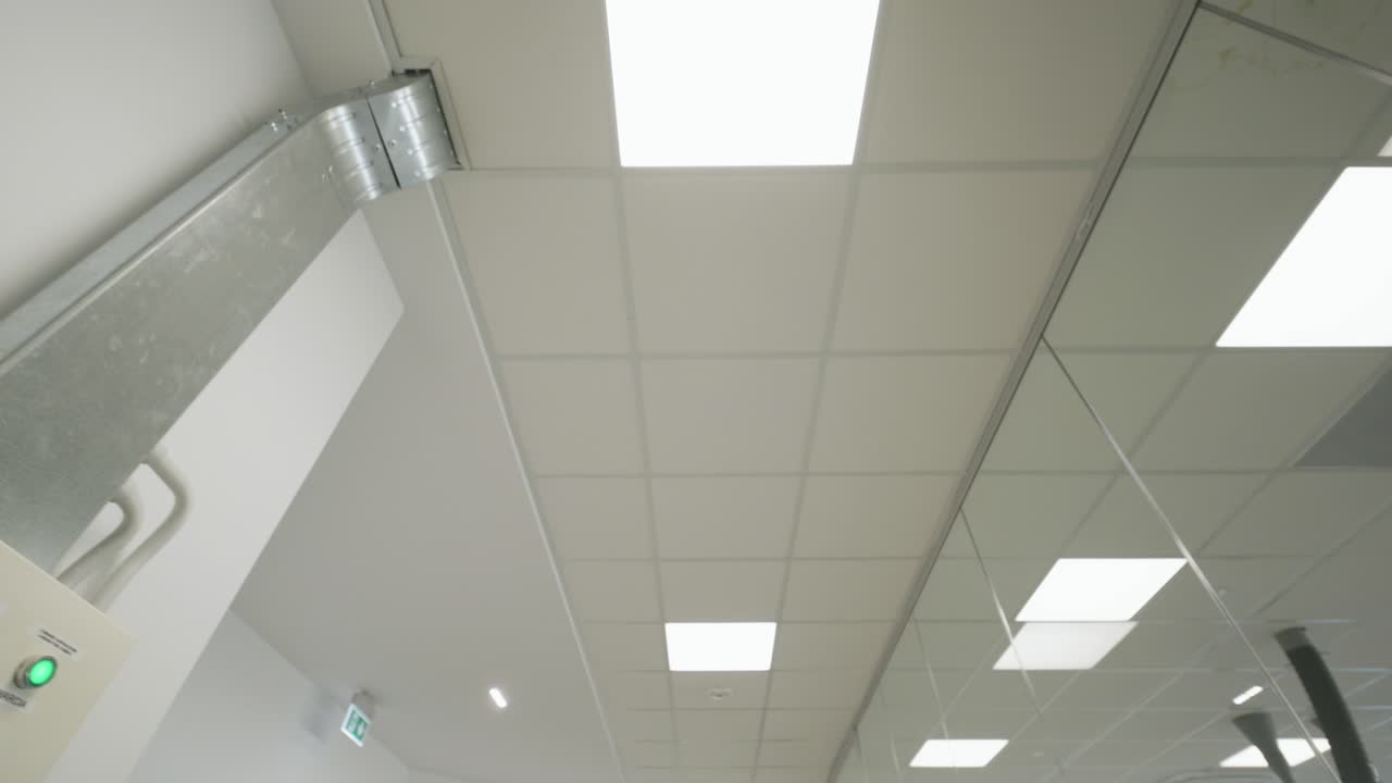 Movimento in avanti della camera sotto un soffitto moderno di un ufficio con luci LED e linee architettoniche pulite. Interni aziendali minimal, illuminazione intensa e atmosfera professionale contemporanea.