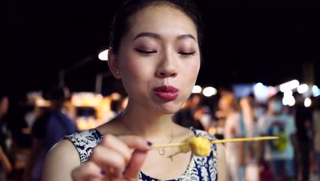 mujer asiática comiendo huevos de codorniz fritos en el mercado nocturno