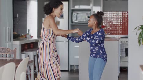 Happy-african-american-mother-and-daughter-dancing-in-kitchen,-slow-motion
