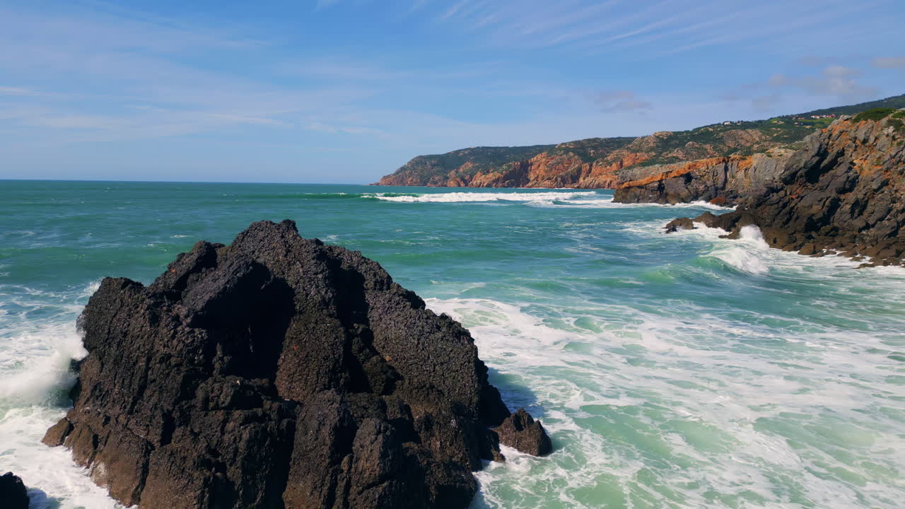 Sunny rocky coastal landscape with blue sea splashing on rough cliffs aerial.