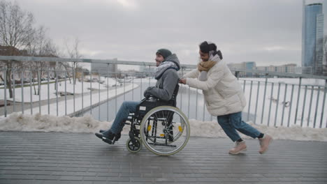 side view of a muslim woman pushing friend on a wheelchair on a slope