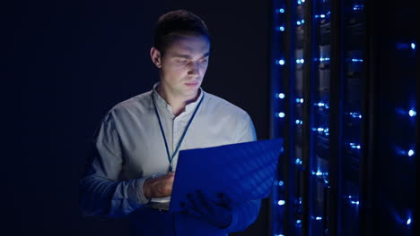 it technician in data center digital server room controlling work of rack server cabinets with a tablet. professional server engineer at work. man technicians working in high tech server rack room