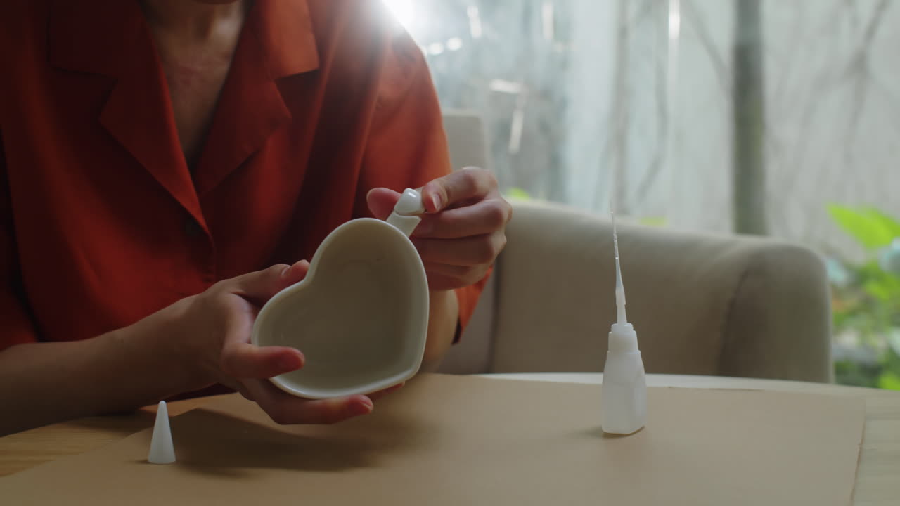Woman Gluing Broken Handle on Mug in Heart Shape