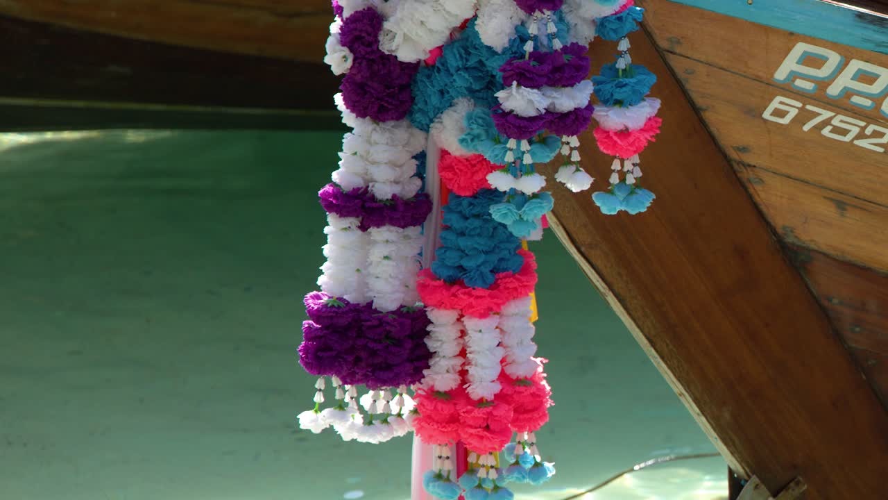 ターコイズブルーの海に浮かぶ木造船に吊るされた、鮮やかな花のガーランドのクローズアップショット