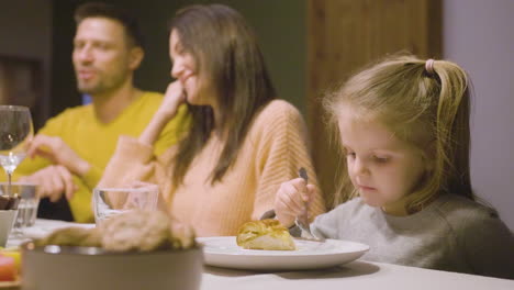 Seitenansicht-Eines-Blonden-Kleinen-Mädchens,-Das-Apfelkuchen-Isst-Und-Am-Tisch-Sitzt,-Während-Ihre-Eltern-Beim-Abendessen-Sprechen