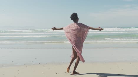 feliz mujer afroamericana con los brazos abiertos en una playa soleada
