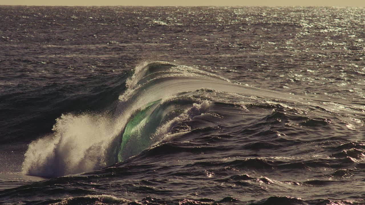 Swirling ocean surface churns as wave folds across frame, soft splash and dusk color