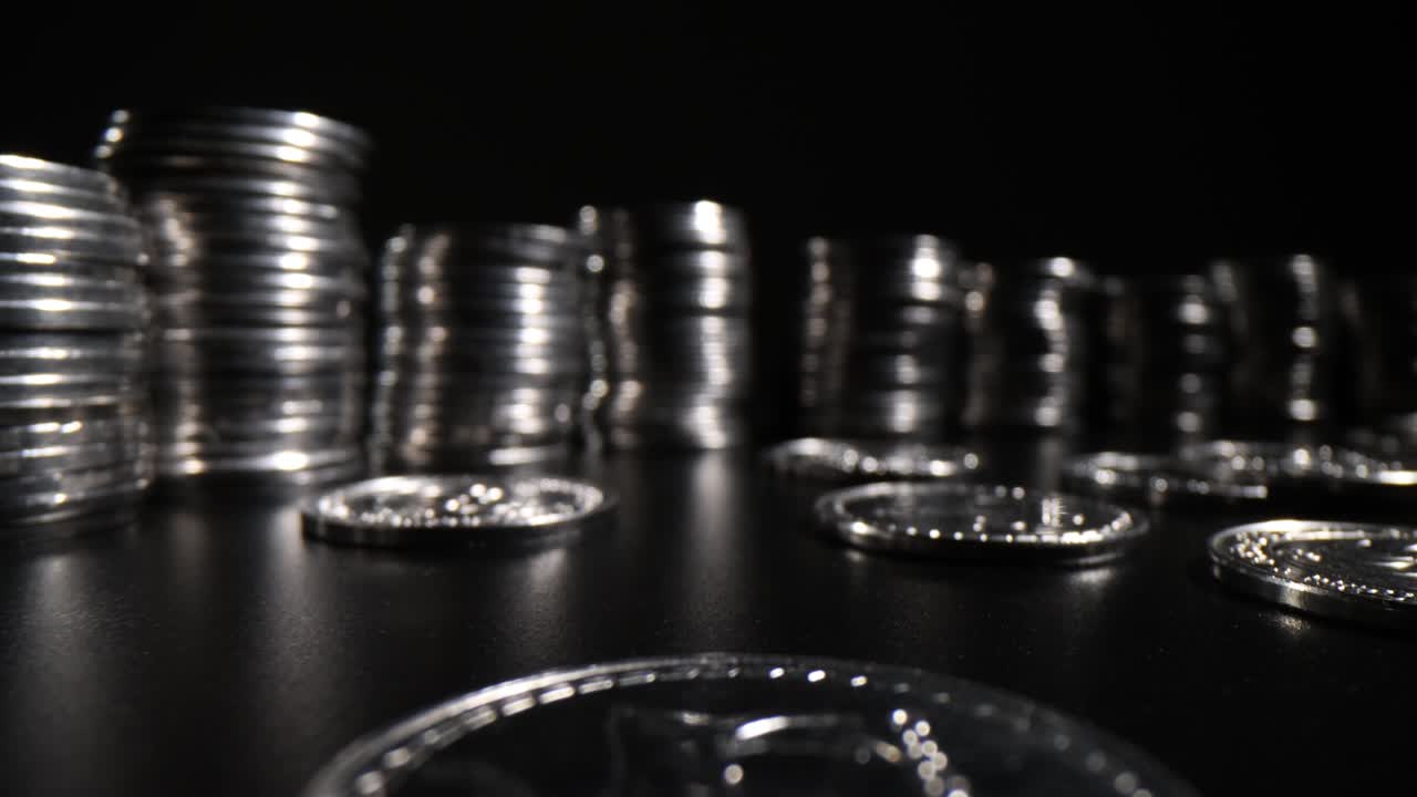 Curve of stacks of silver coins on black table in dark premise