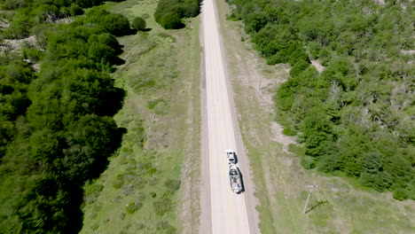 aerial flying over road through valley floor with car and attached boat trailer passing through